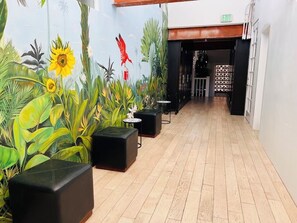 A hallway with a mural of tropical plants and a red bird, leading to a room with a black partition and a small table.