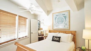 A bedroom with a bed, a ceiling fan, a nightstand, a lamp, and a framed picture on the wall. - Historic Suites Hotel in Walkable Downtown between Siesta & Lido Beaches (Sarasota)