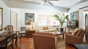 A living room with a sofa, two armchairs, a coffee table, a TV, and a ceiling fan. - Historic Suites Hotel in Walkable Downtown between Siesta & Lido Beaches (Sarasota)