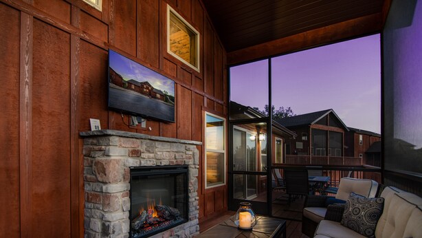 A cozy living room with a stone fireplace, comfortable seating, and large windows overlooking a deck. - Private hot tub-close to community pool-Pet frndly (Reeds Spring)