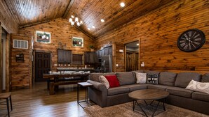 A cozy cabin interior with a wooden interior, a dining area, and a living room with a large clock on the wall. - Private hot tub-close to community pool-Pet frndly (Reeds Spring)