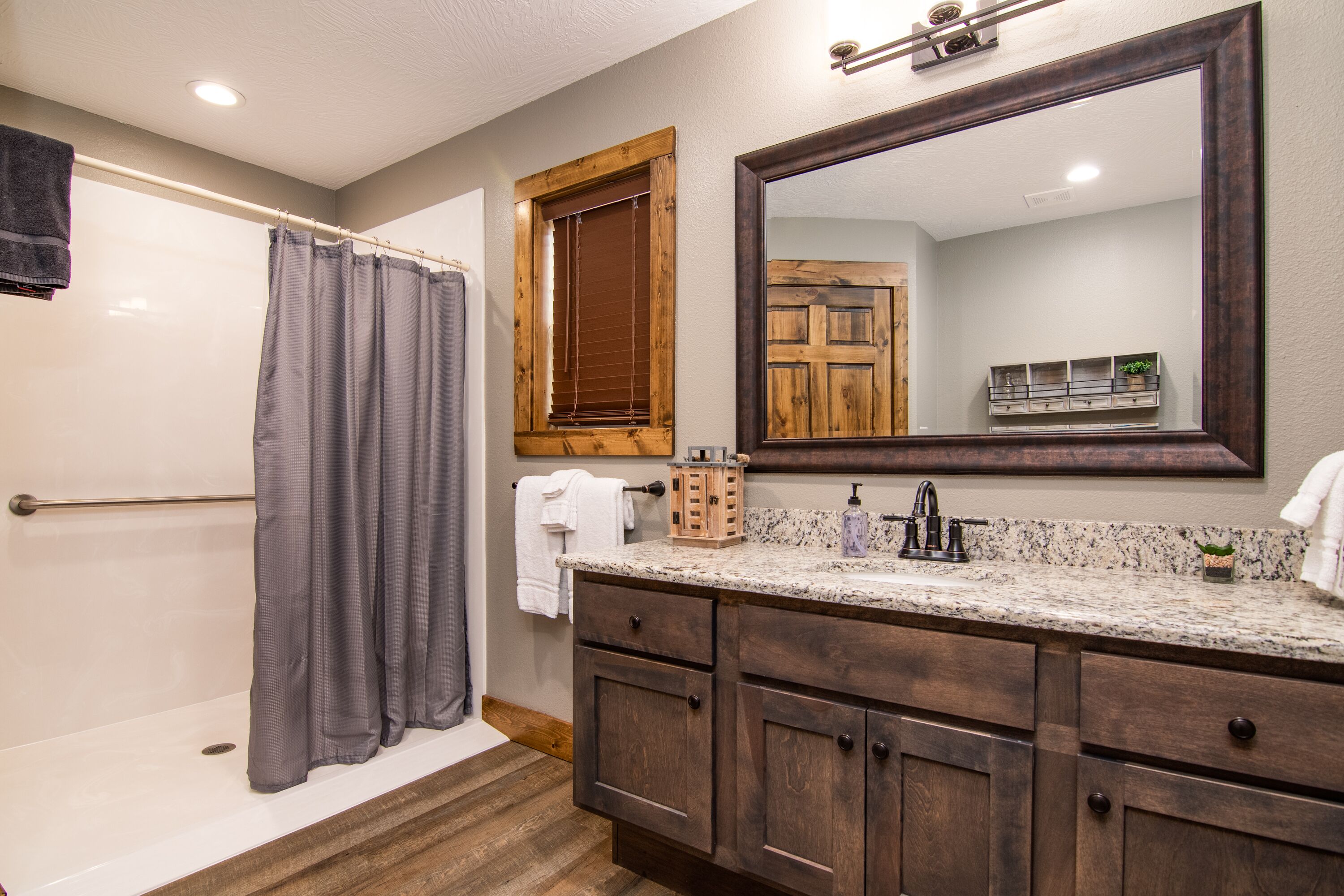 A bathroom with a bathtub, a shower curtain, a large mirror, wooden cabinets, and a granite countertop.