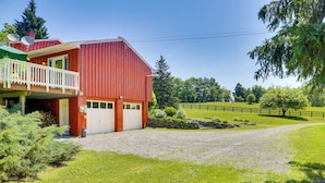 Ein rotes Bauernhaus mit weißem Balkon, einer Schotterauffahrt und einem eingezäunten Weidegrundstück.
