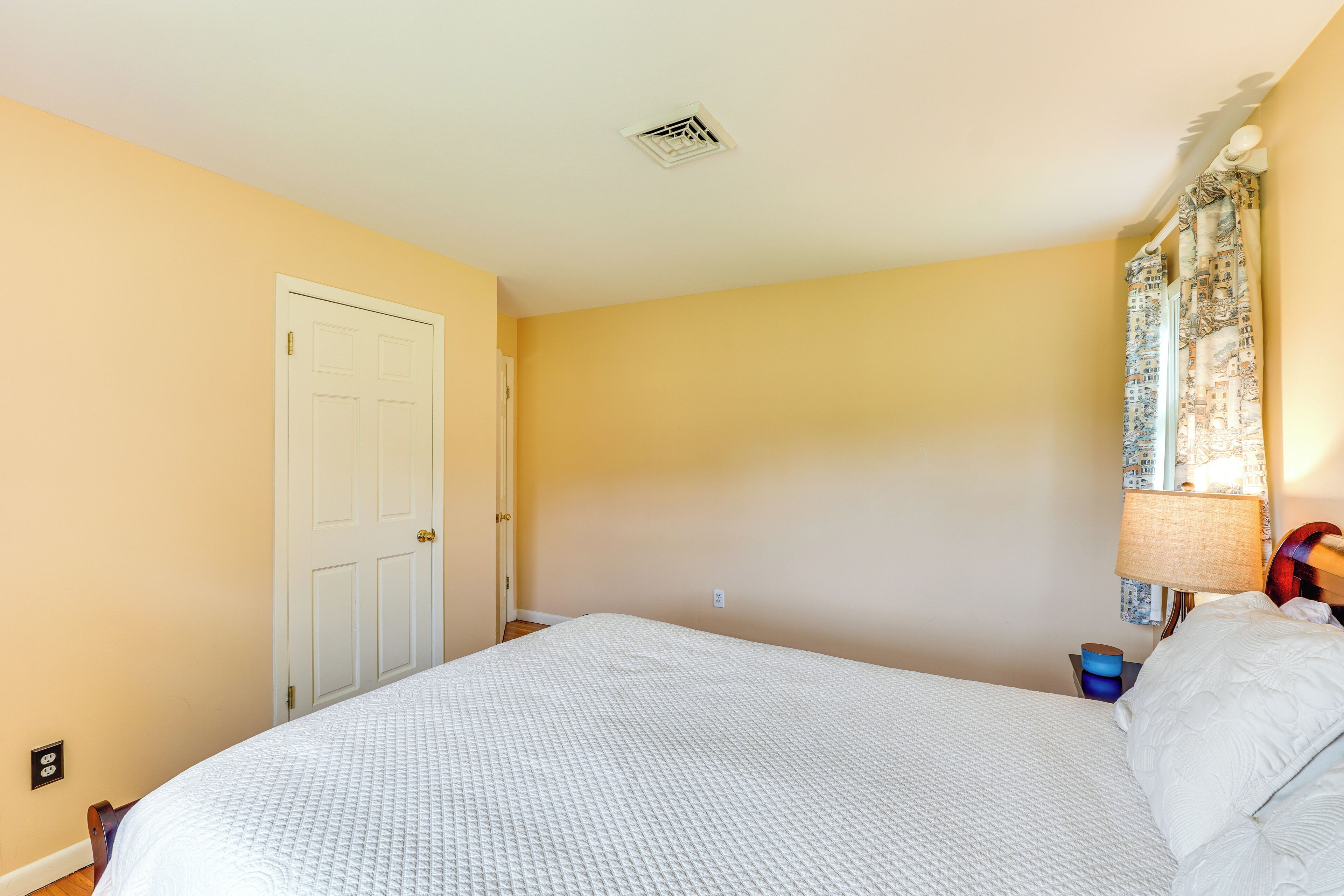 Una camera da letto con un letto, una porta, una presa elettrica e un comodino con una lampada.
