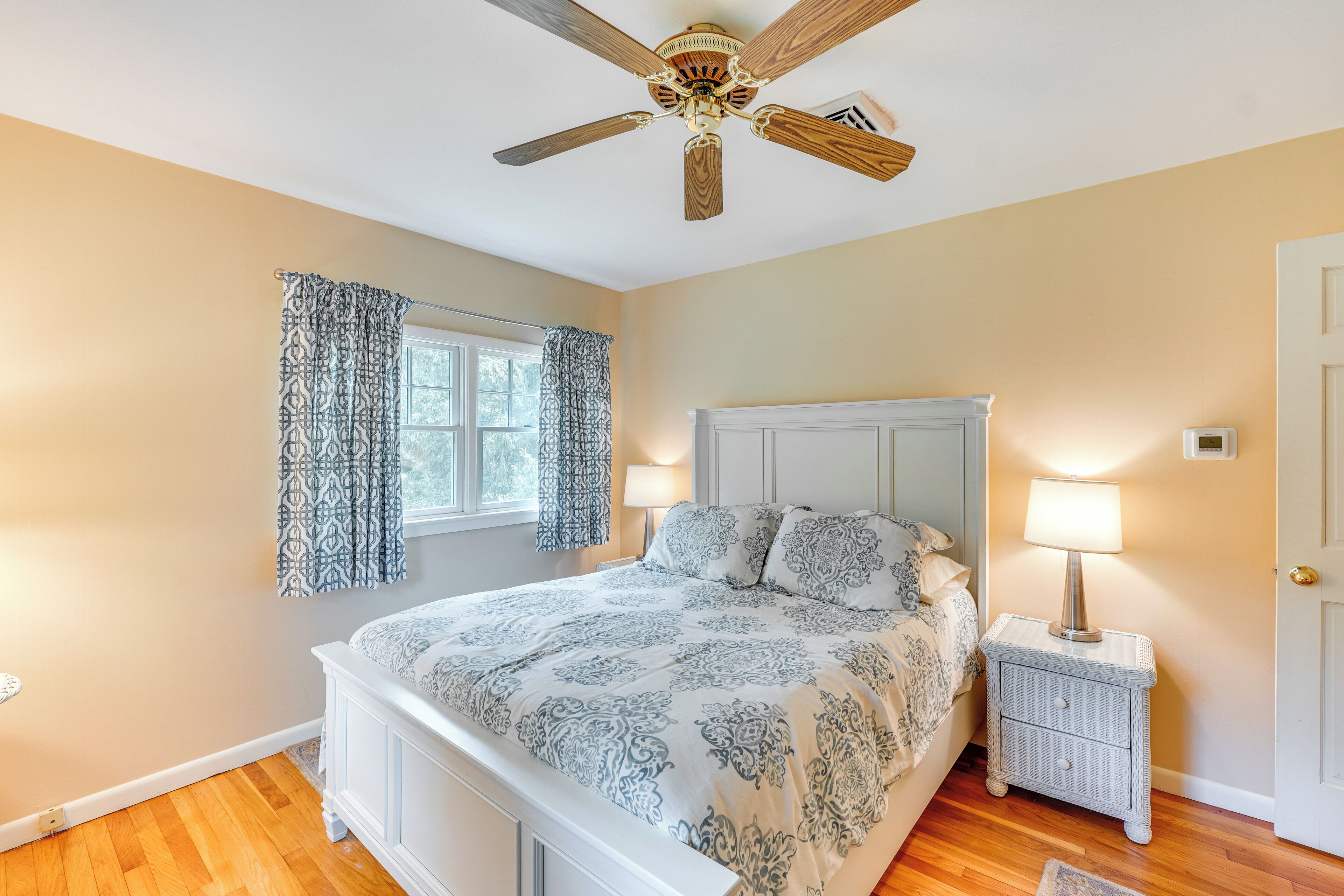 A bedroom with a bed, a nightstand, a ceiling fan, and a window with curtains.