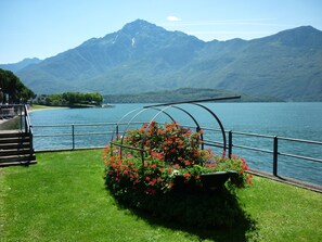 Ein Garten am See mit einem Metallbogen, einer Holztreppe und einem Blick auf die Berge.