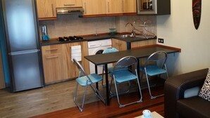 A compact kitchen with wooden cabinets, a built-in oven, a microwave, and a sink. There is a dining table with four chairs.