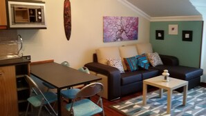 A compact living space with a kitchenette, a dining area with chairs, a sofa with cushions, and a painting on the wall. - Apartment with terrace, and views of the sea and the mountains in Sonabia (Castro Urdiales)
