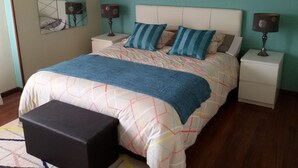 A bedroom with a bed, two bedside tables, a nightstand, a black ottoman, a wall-mounted mirror, and a beach-themed painting. - Apartment with terrace, and views of the sea and the mountains in Sonabia (Castro Urdiales)