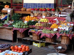 A fruit and vegetable market stall with various produce displayed in baskets and crates, with price tags visible. - BHF Residences Bordadeira (Calheta)