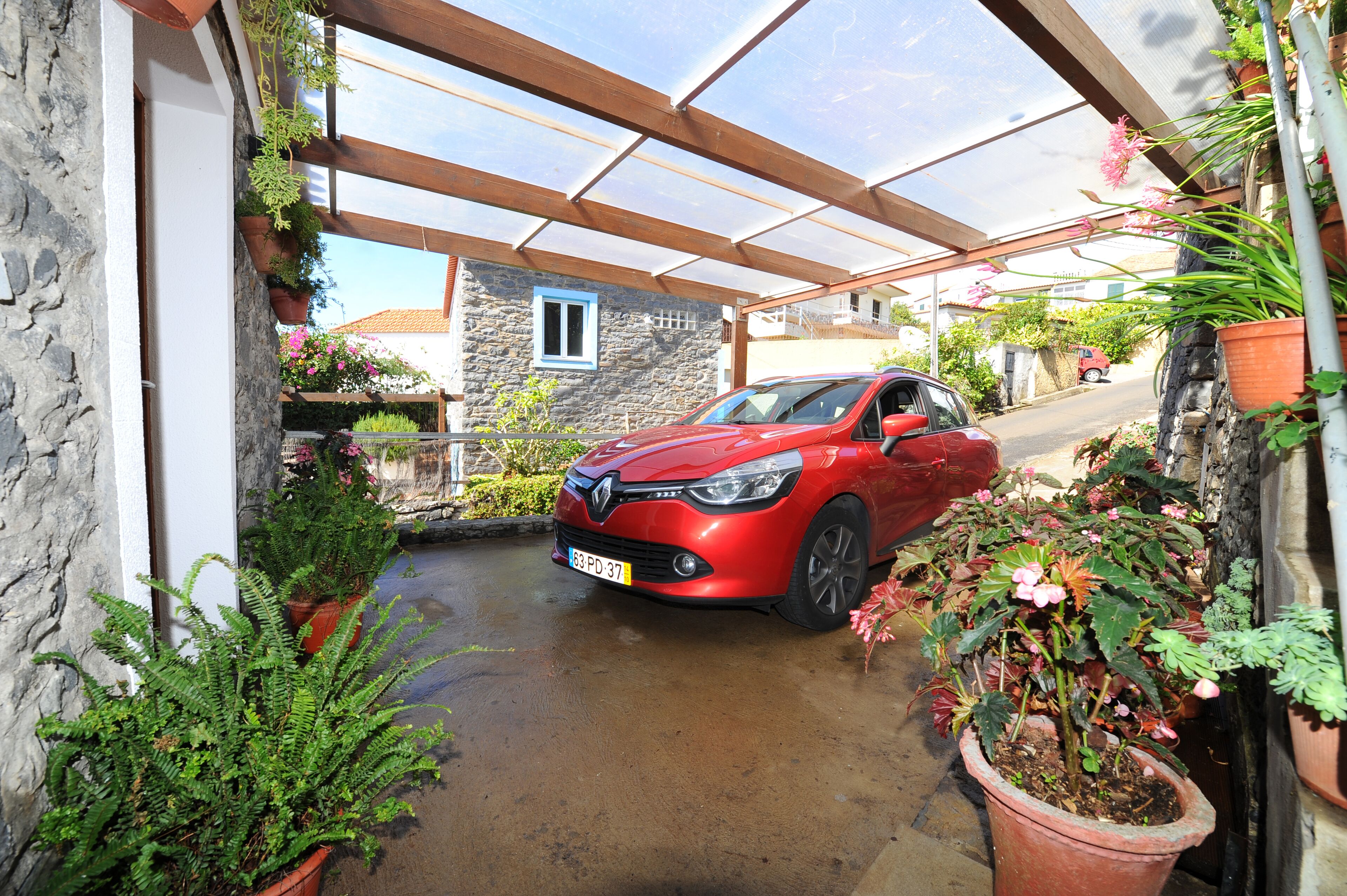 A red car parked under a covered area with stone walls and potted plants.