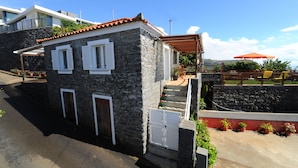 Un bâtiment en pierre avec un toit recouvert de tuiles rouges, des volets blancs et un petit porche doté d’une balustrade en bois.