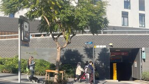 A street scene with a tree, a bench, and a building with a parking garage entrance. - SUNNY ATTIC, 2 TERRACES, PRIVATE SOLARIUM, 3 ROOM, 2 BATHS. 3 MIN TO SUBWAY. (Barcelona)