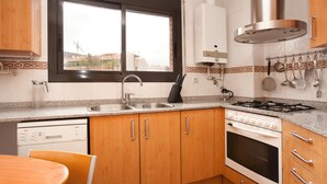 A kitchen with wooden cabinets, a dishwasher, a stove, and a window with a view of buildings. - SUNNY ATTIC, 2 TERRACES, PRIVATE SOLARIUM, 3 ROOM, 2 BATHS. 3 MIN TO SUBWAY. (Barcelona)