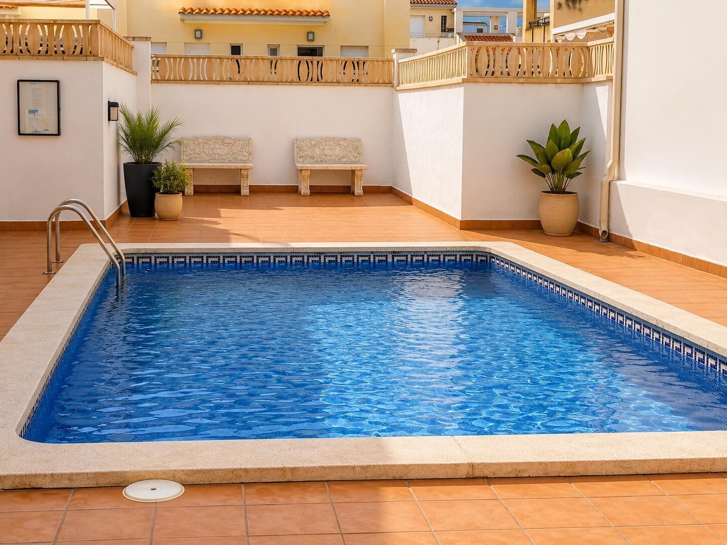 Una piscina rectangular con borde de azulejos, rodeada por un suelo alicatado y una valla de madera.