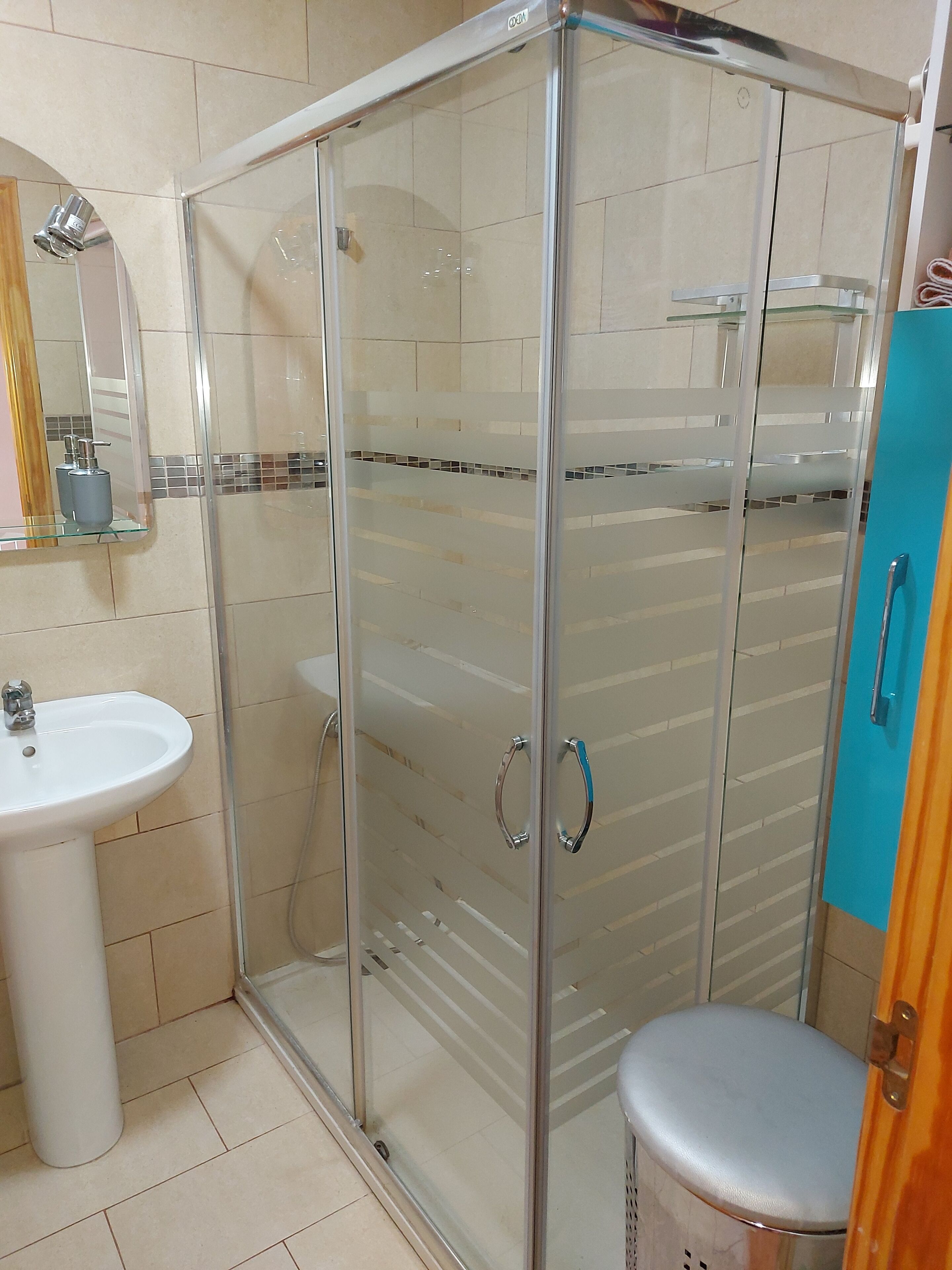A bathroom with a glass-enclosed shower, a white sink, and a blue cabinet.