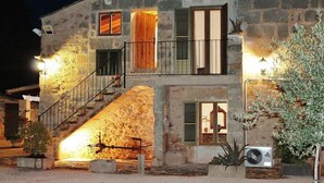 Un edificio in pietra con una scala, diverse finestre con persiane, illuminazione esterna e piante in vaso.