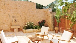 Patio esterno con pareti in pietra, tavolo di legno, sedie bianche imbottite e piante in vaso.