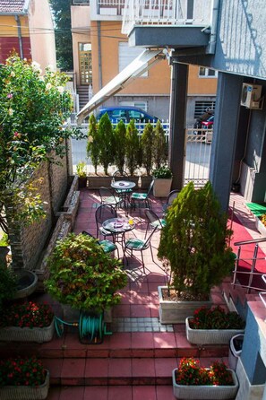 An outdoor patio with tables and chairs, surrounded by potted plants and a red-tiled floor. - Guest Accommodation Majesty (Niš)