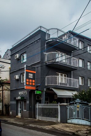 A multi-story building with balconies, a cafe, and a gated entrance. - Guest Accommodation Majesty (Niš)