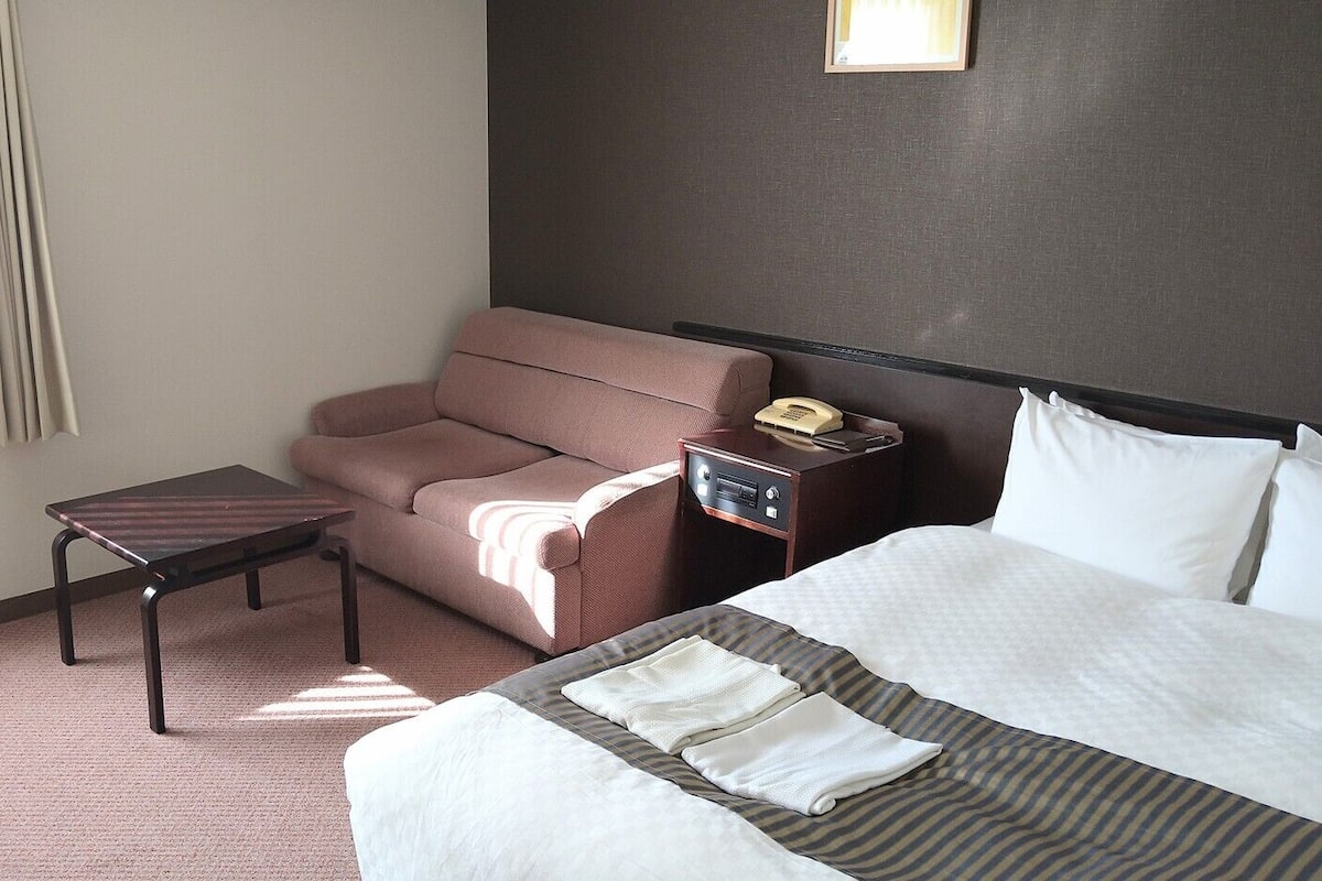 Ein Hotelzimmer mit Bett, einer Couch, einem kleinen Tisch, einem Nachttisch mit Telefon und einer Wandleuchte.