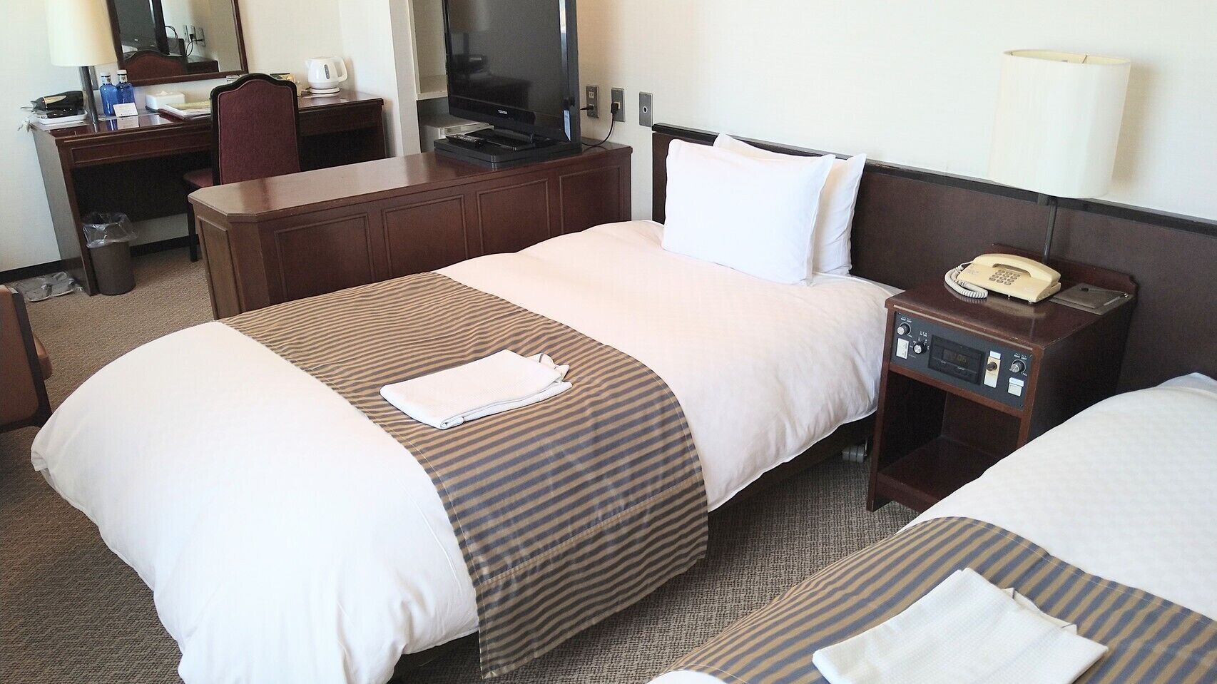 A hotel room with a bed, a desk, a television, and a telephone.