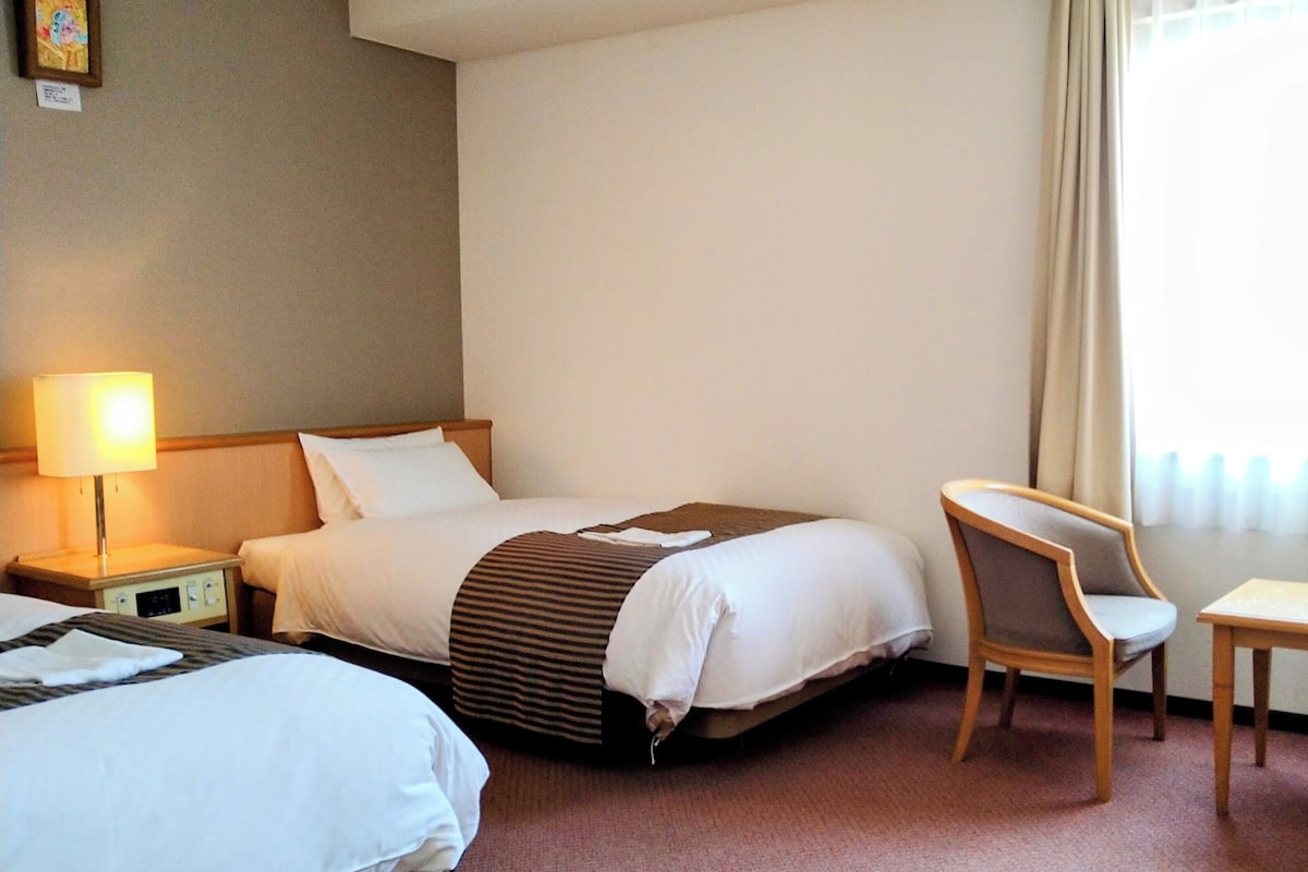 Ein Hotelzimmer mit Bett, Stuhl, Nachttisch und Lampe.