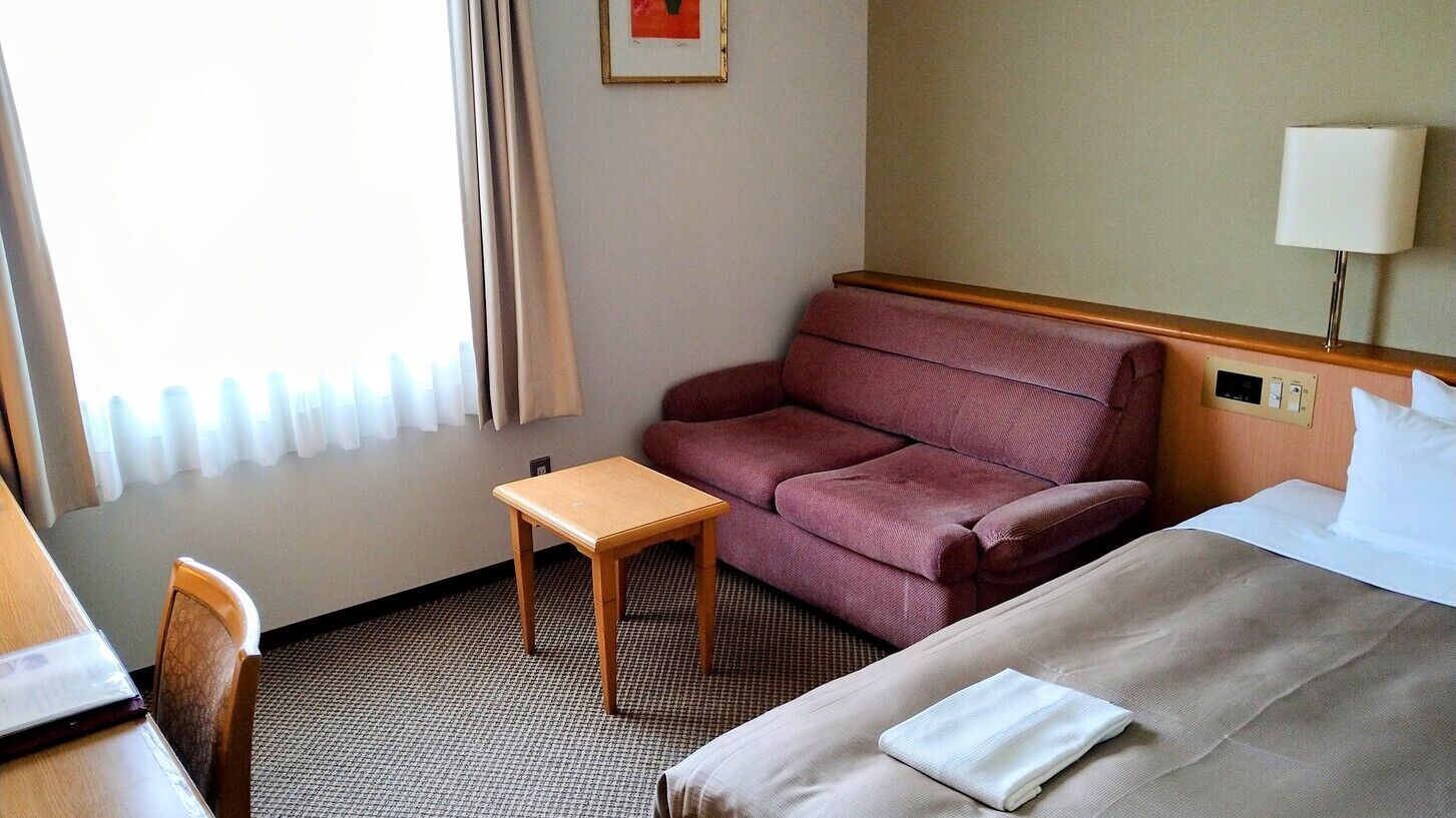 A hotel room with a bed, a small table, a sofa, and a lamp.