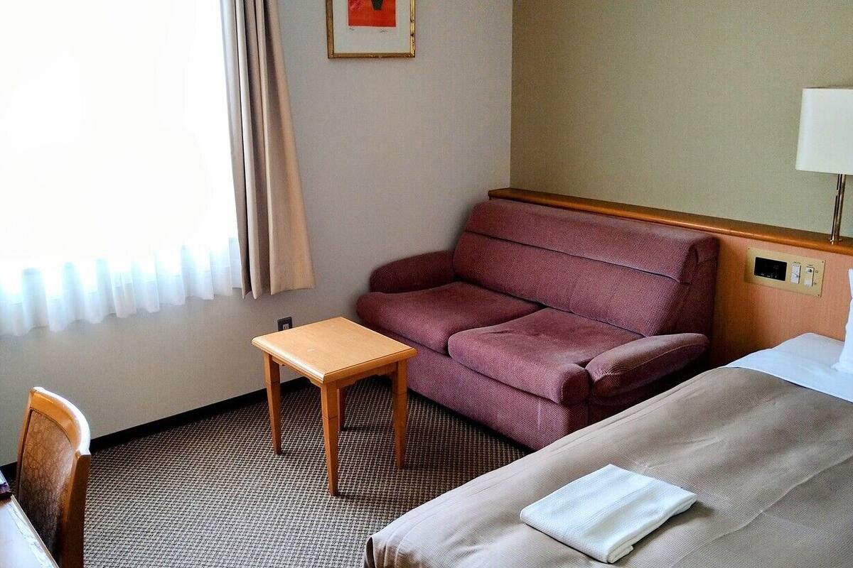 Ein Hotelzimmer mit Bett, einem kleinen Tisch, einer Couch und einer Lampe.