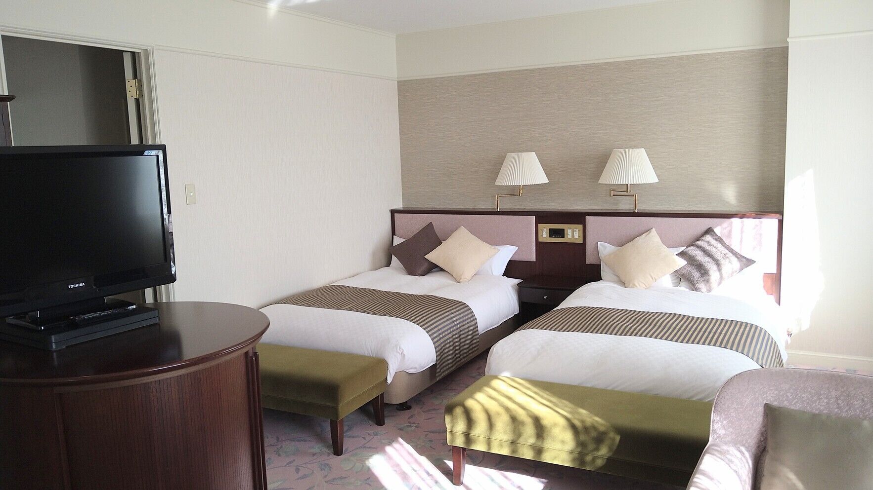 A hotel room with two beds, a TV, bedside lamps, and a small table.