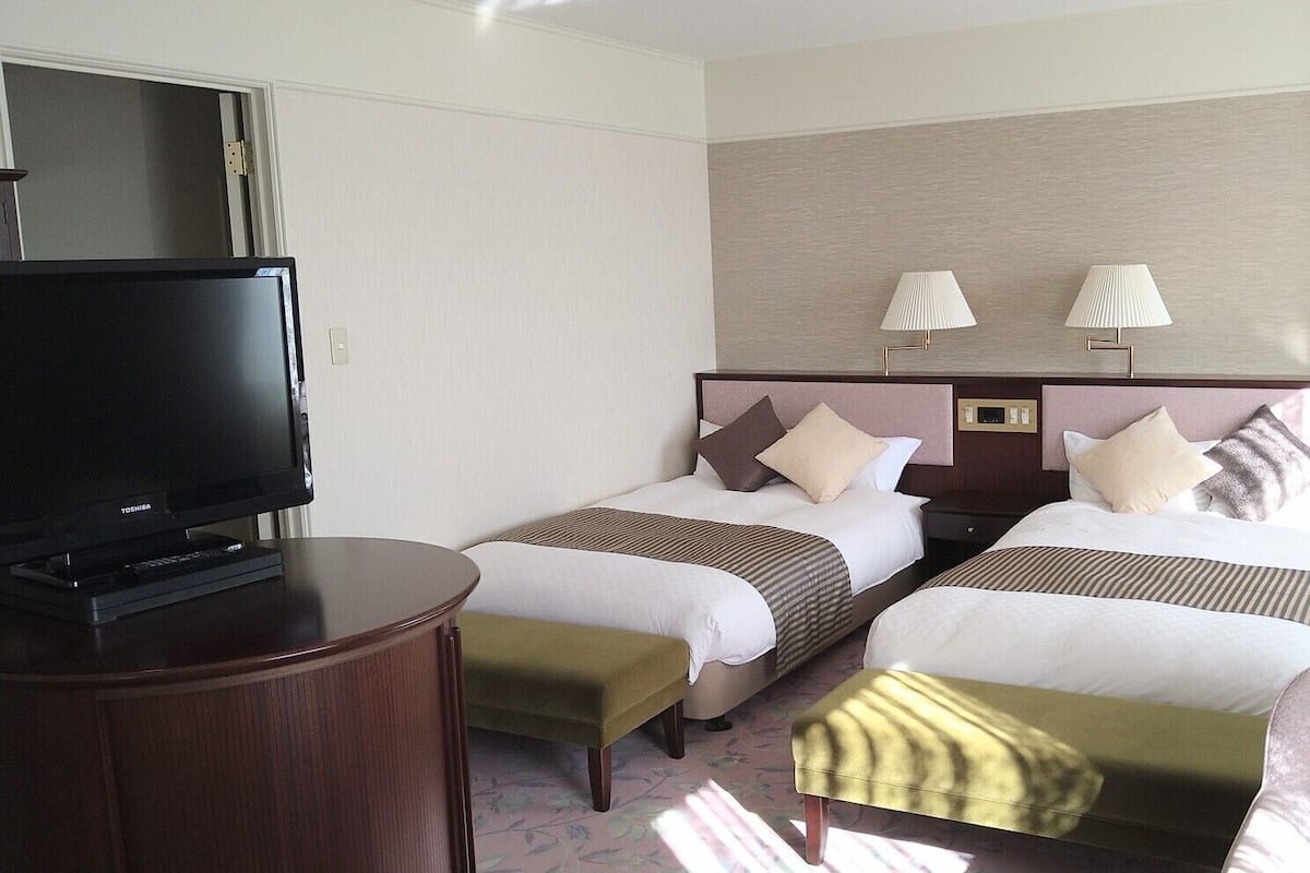 Ein Hotelzimmer mit zwei Betten, einem Fernseher, Nachttischlampen und einem kleinen Tisch.