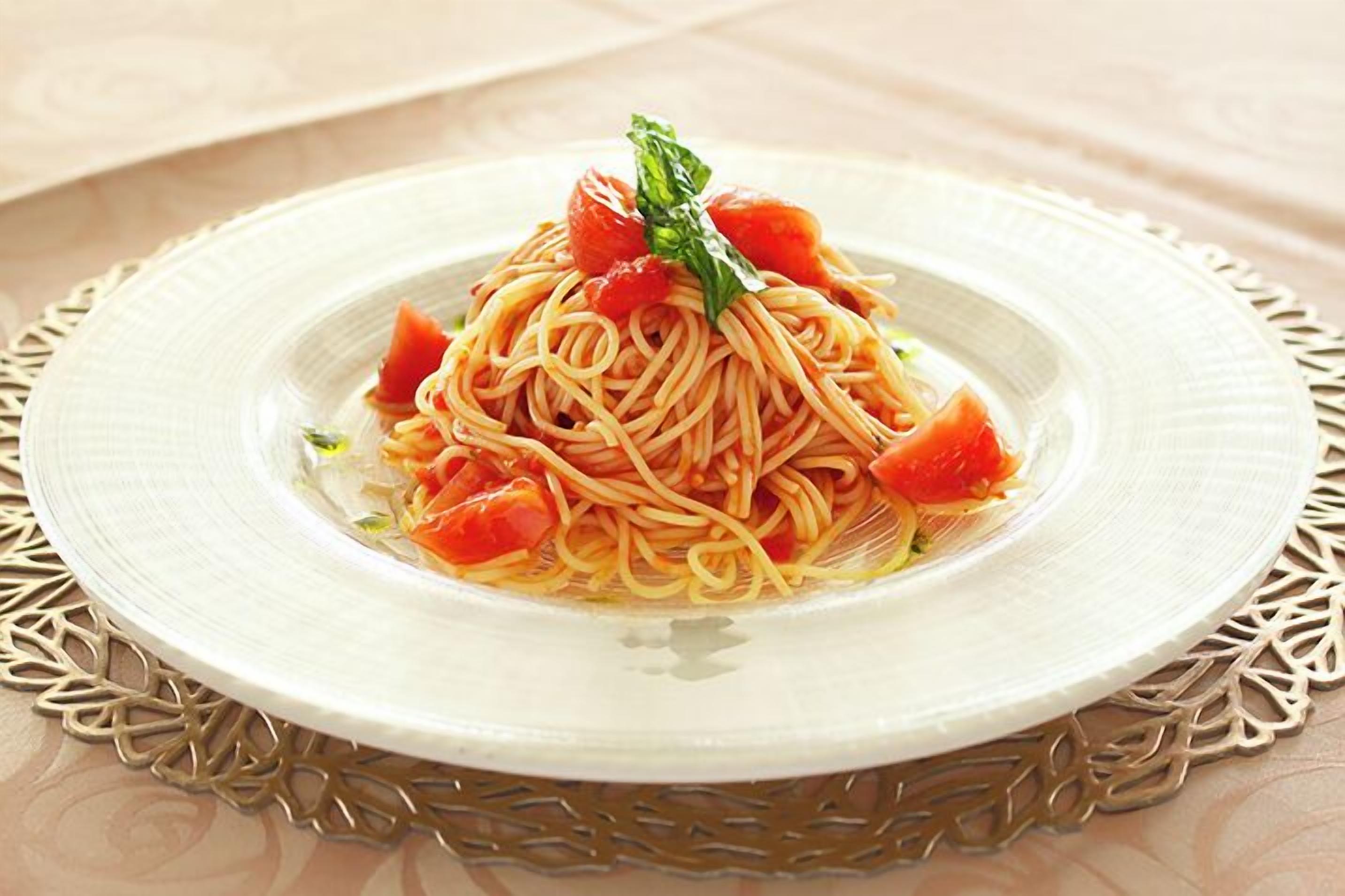 A plate of spaghetti with tomato pieces and a basil leaf garnish.
