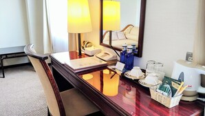 Ein Hotelzimmer mit Holzschreibtisch, Stuhl, Telefon, Spiegel, Nachttisch mit Toilettenartikeln und einem Fenster mit Vorhängen.