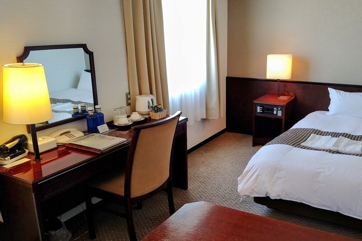 Ein Hotelzimmer mit Bett, Schreibtisch mit Lampe, Telefon und Nachttisch mit Lampe.