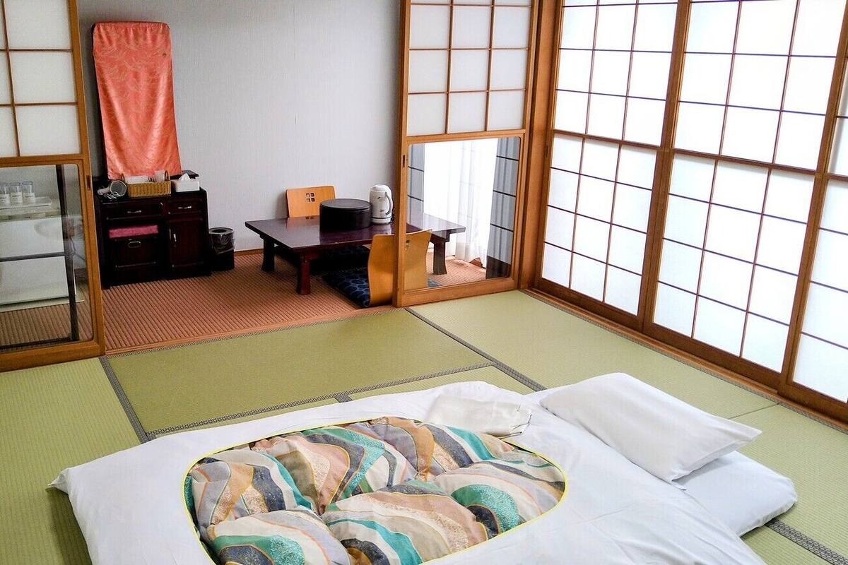 Ein traditioneller japanischer Raum mit Tatami-Bodenbelag, einem Futon, einem niedrigen Tisch mit Wasserkocher und verschiebbaren Türen.