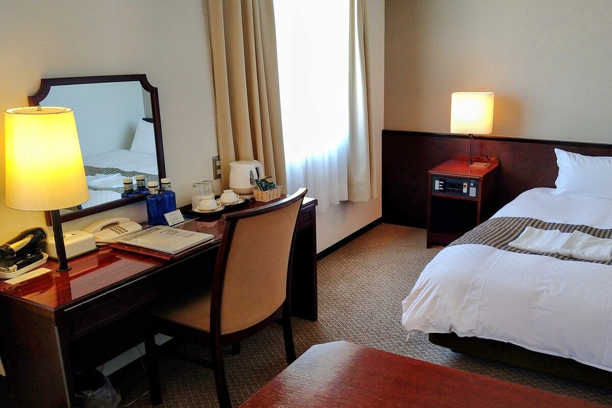 Ein Hotelzimmer mit Bett, Schreibtisch mit Lampe, Telefon und Nachttisch mit Lampe.