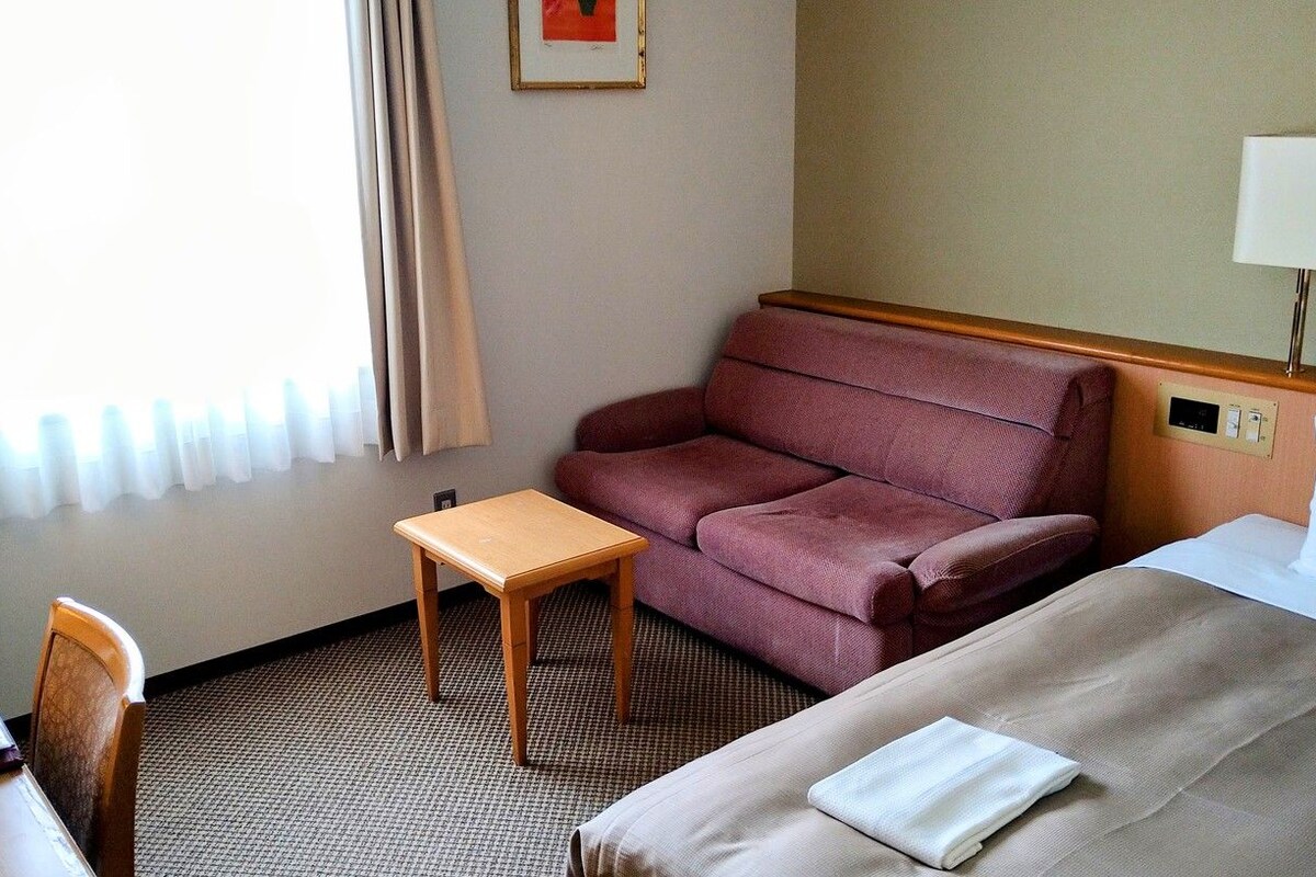 A hotel room with a bed, a small table, a sofa, and a lamp.