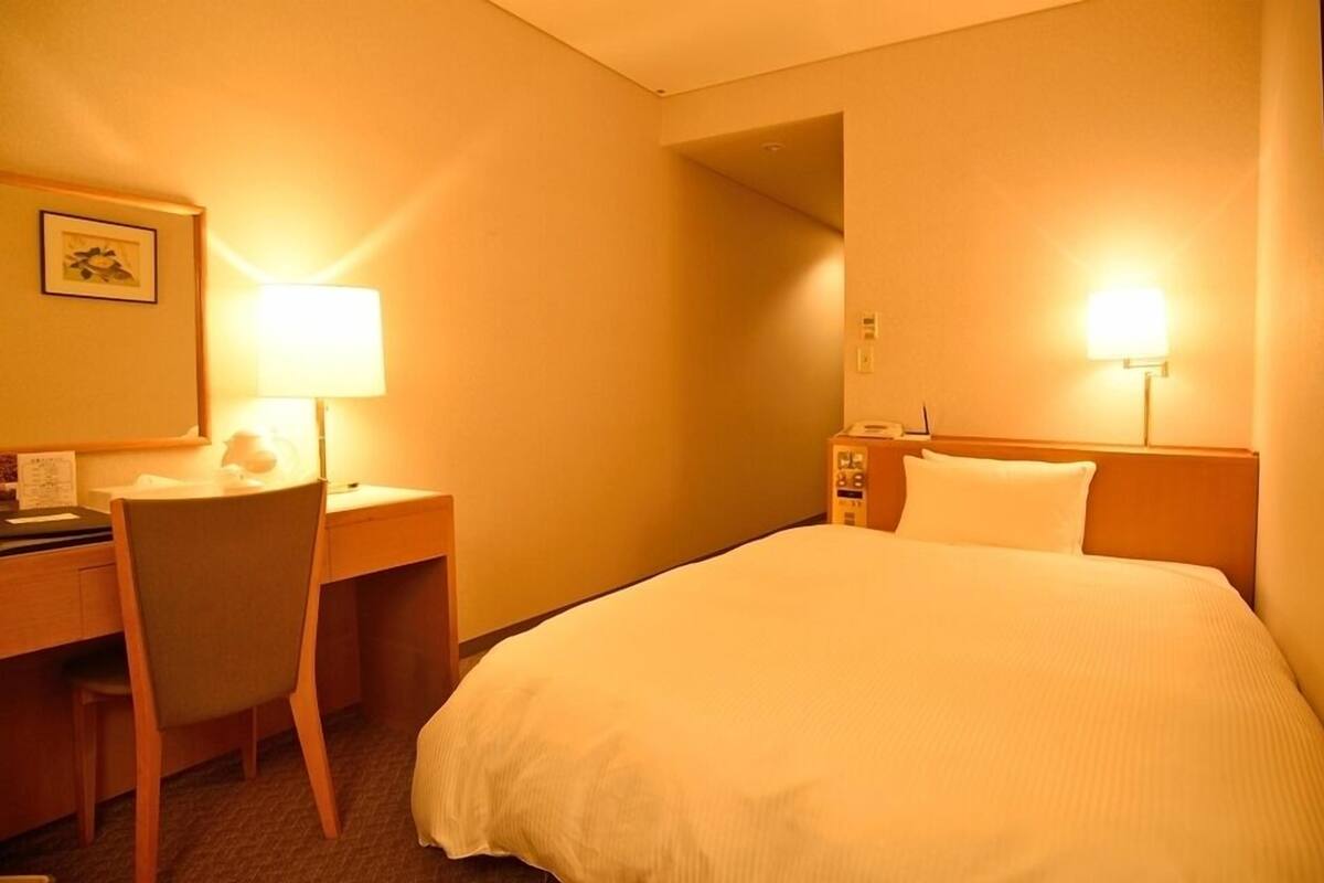 Ein Hotelzimmer mit Bett, Schreibtisch, Stuhl und zwei Wandlampen.