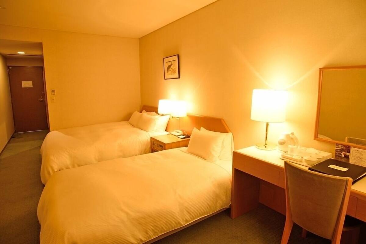 Ein Hotelzimmer mit zwei Betten, einem Schreibtisch mit Stuhl, einer Lampe und einem Spiegel.