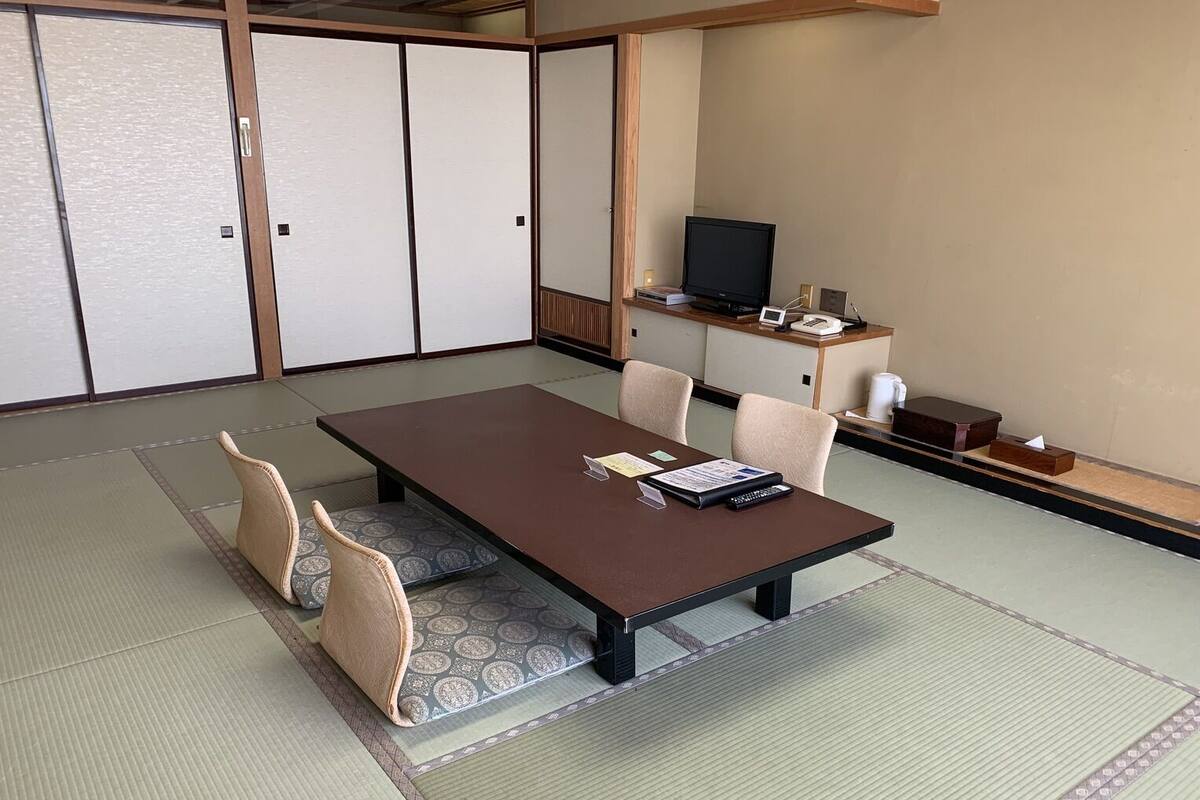 Ein traditioneller japanischer Raum mit Tatami-Bodenbelag, einem niedrigen Tisch und einem Fernseher auf einem Holzständer.