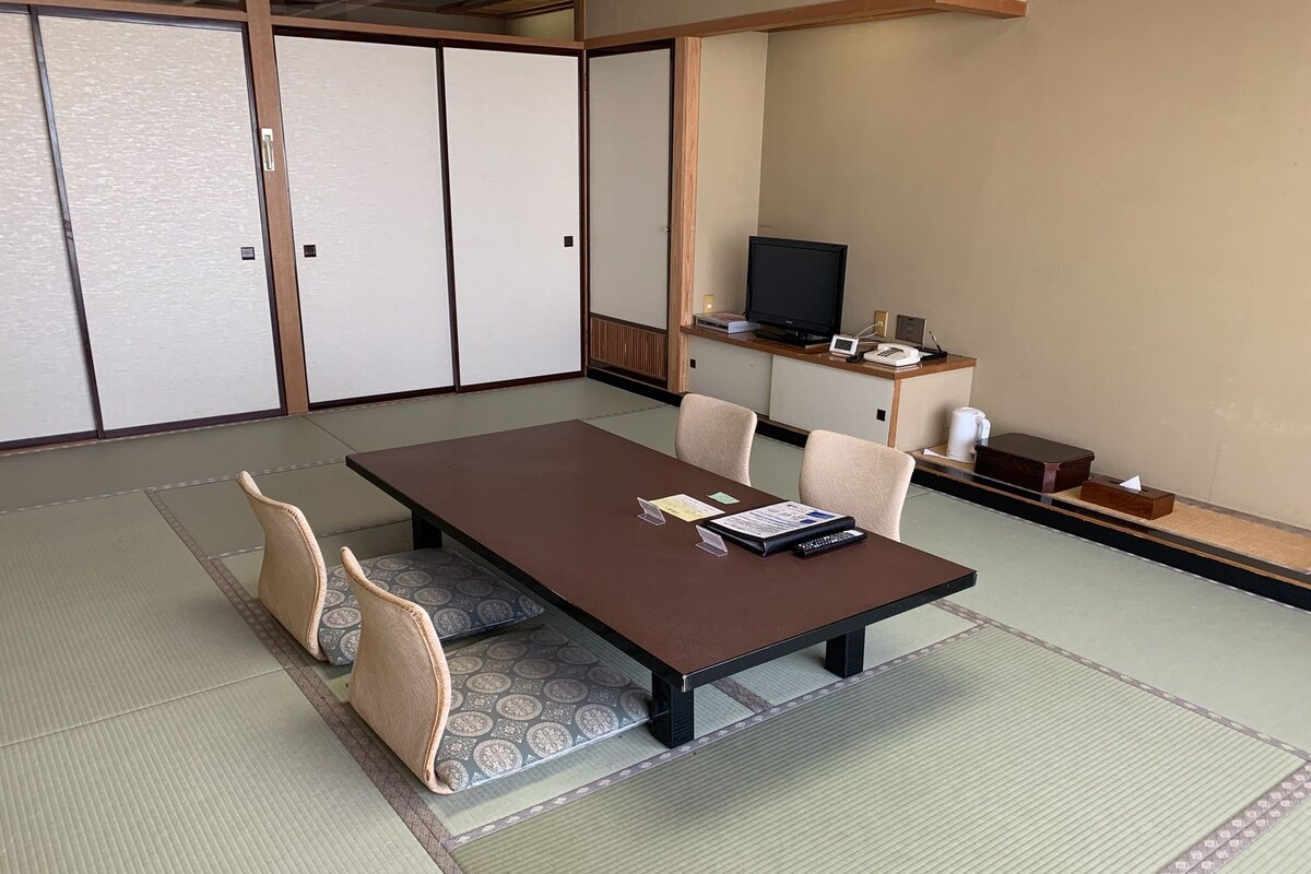 A traditional Japanese-style room with tatami flooring, a low table, and a television on a wooden stand.