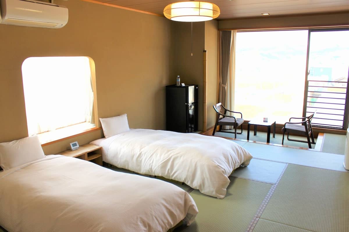 Ein Hotelzimmer mit zwei Betten, einem Kühlschrank, einem kleinen Tisch und einem Sessel.