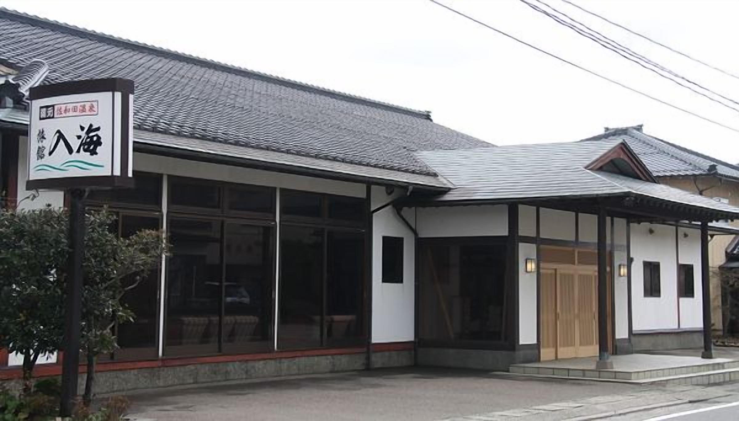 A traditional Japanese building with a signboard, large windows, and a tiled roof.