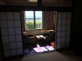 Una habitación con suelo de tatami, una mesa baja, un sofá y vistas a un cuerpo de agua a través de una ventana.