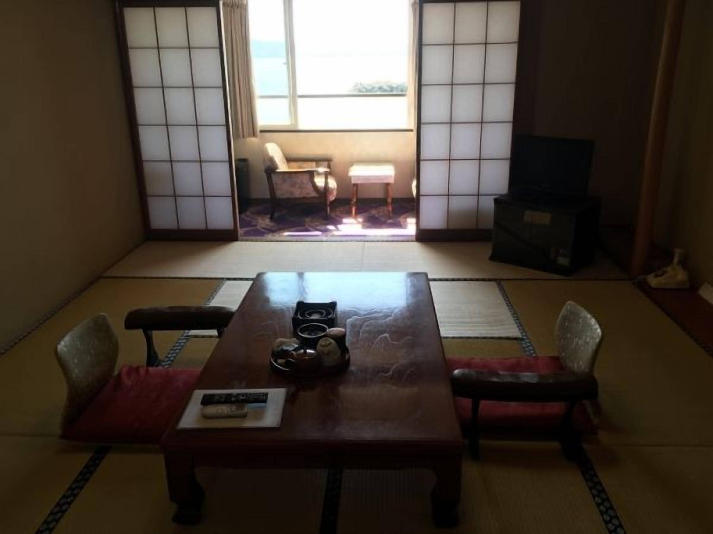 A traditional Japanese room with tatami flooring, a low table with cushions, a television, and sliding doors.