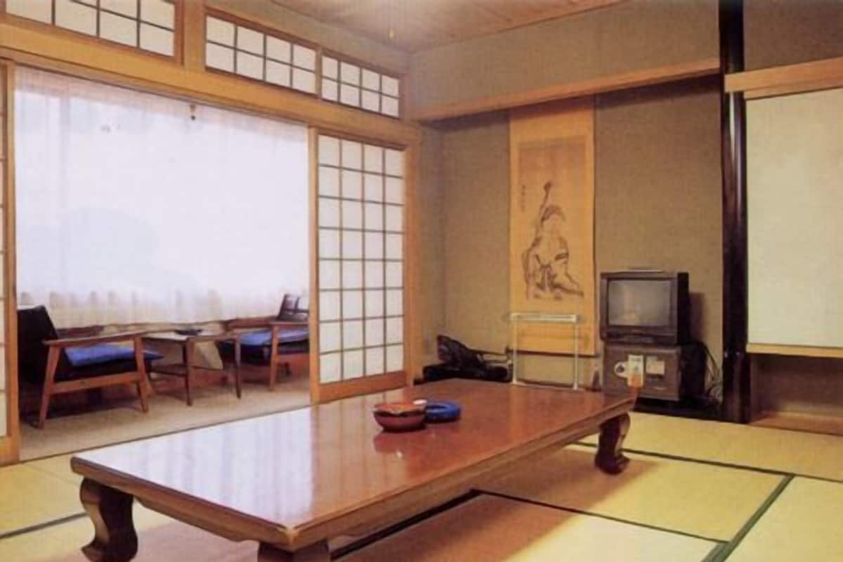 A traditional Japanese tatami room with a low wooden table, tatami mats, a television, and a shoji screen.