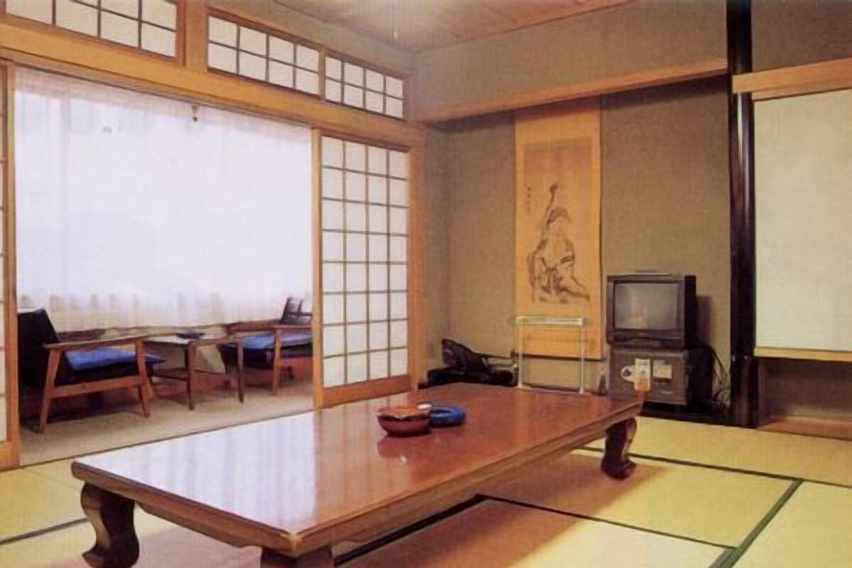 Ein traditioneller japanischer Raum mit Tatami-Matten, einem niedrigen Holztisch, einem Fernseher und einem Shoji-Bildschirm.