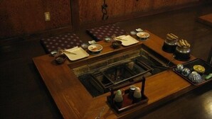 Ein traditioneller japanischer Raum mit Tatami-Böden, einem niedrigen Tisch mit eingebautem Herd und verschiedenen Geschirrgegenständen.