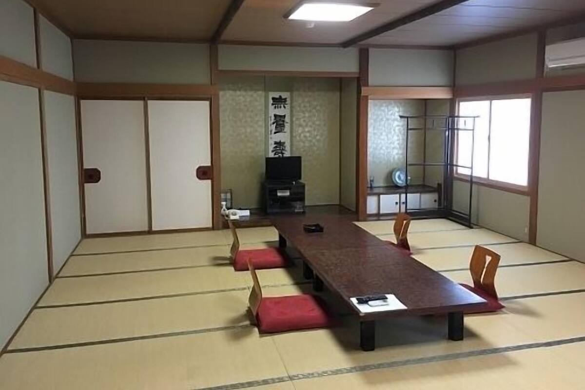 A traditional tatami room with a low table and chairs, a sliding door, and a television.