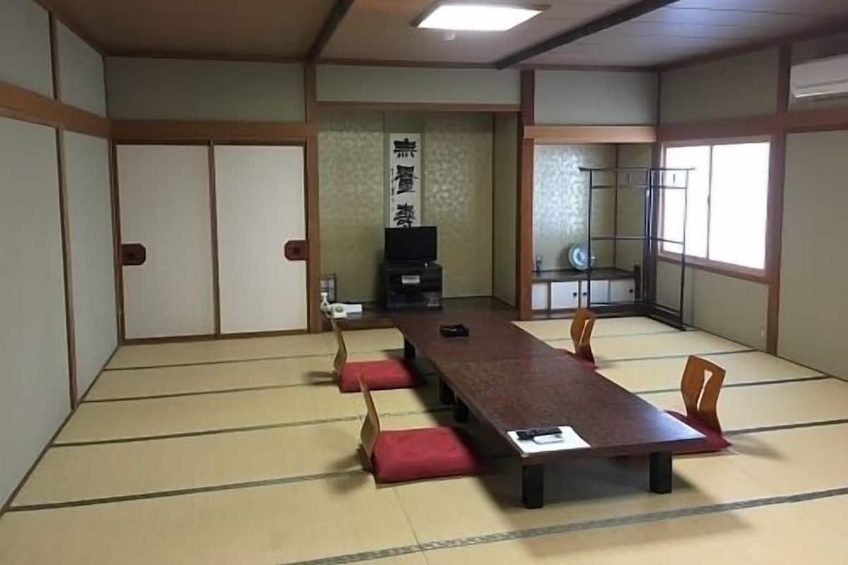 Ein traditioneller Tatamiraum mit niedrigem Tisch, Stühlen, einer Schiebetür und einem Fernseher.
